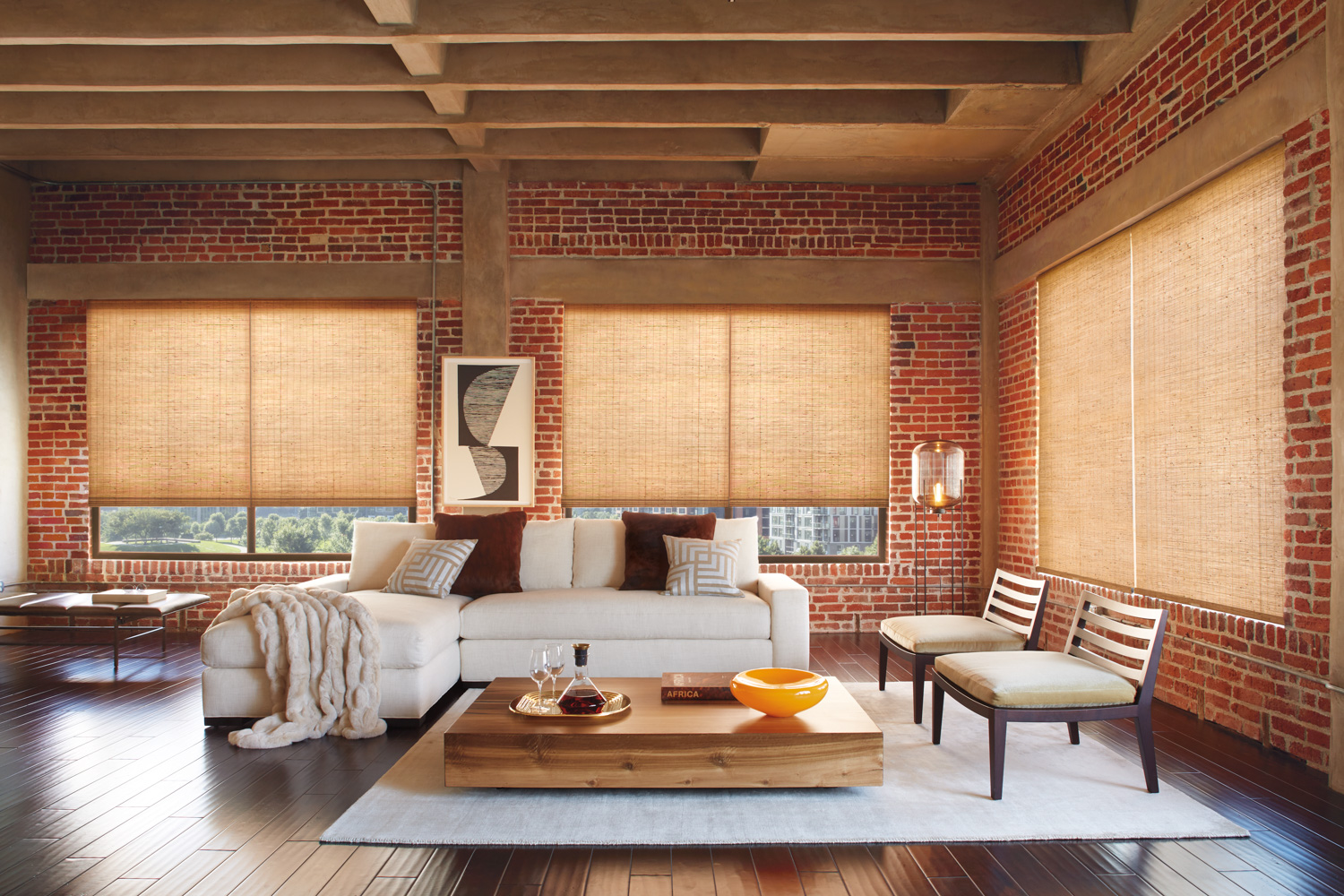 Living room with brick walls, wooden floors, and NATURAL WOVEN WOOD ROMAN SHADES.
