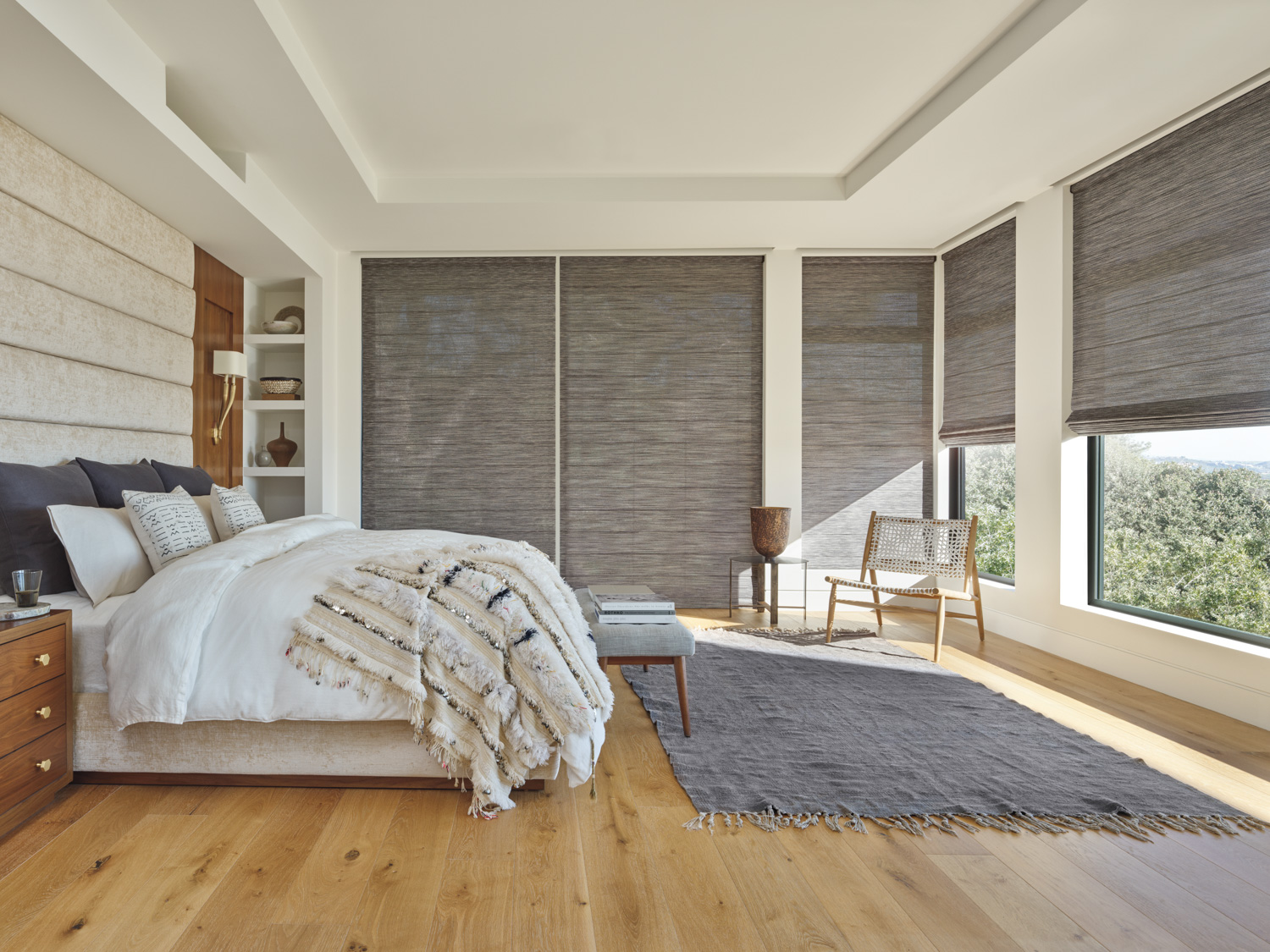 Master bedroom showcasing bed, chair, and window with Hunter Douglas Alustra® Woven Textures® Roman Shades.