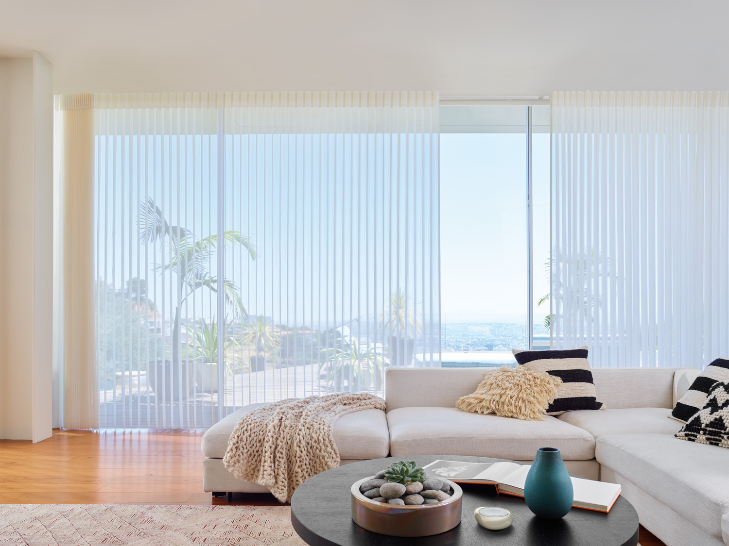 A bright living room with white furniture and floor-to-ceiling windows, highlighting Hunter Douglas Luminette® Sheer Panels.