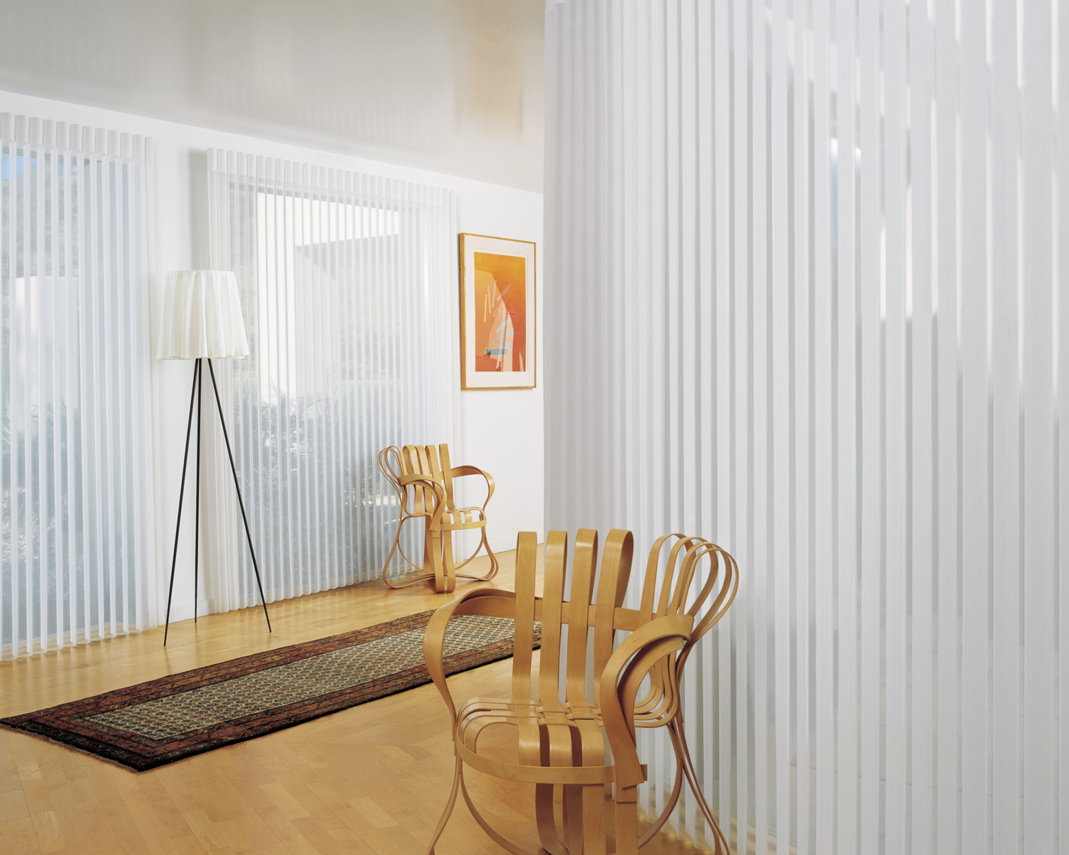 A room with a chair and a rug in front of a window, featuring Hunter Douglas Luminette® Sheer Panels.