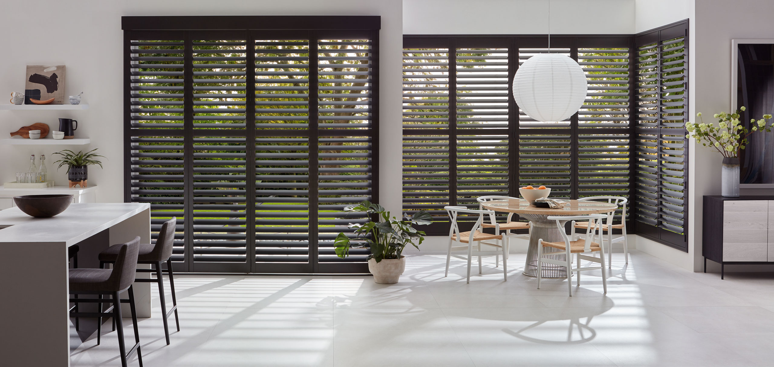 A kitchen with black shutters and a dining table. Hunter Douglas Heritance wood shutters add elegance to the room.