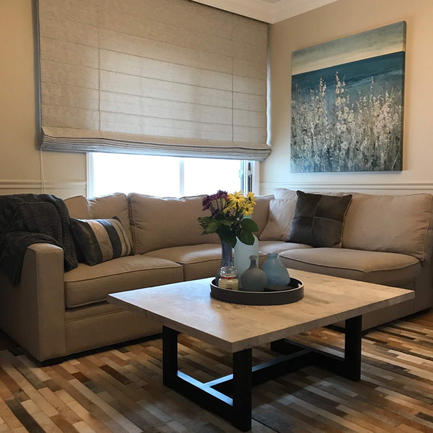 A cozy living room with a couch, coffee table, and a painting. The room is adorned with Fabric Roman Shades.