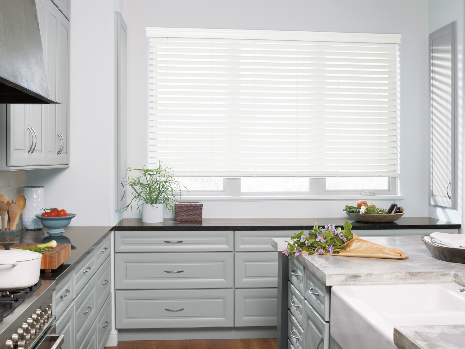 A kitchen with white cabinets and a window featuring Hunter Douglas EverWood® Faux Wood Blinds.
