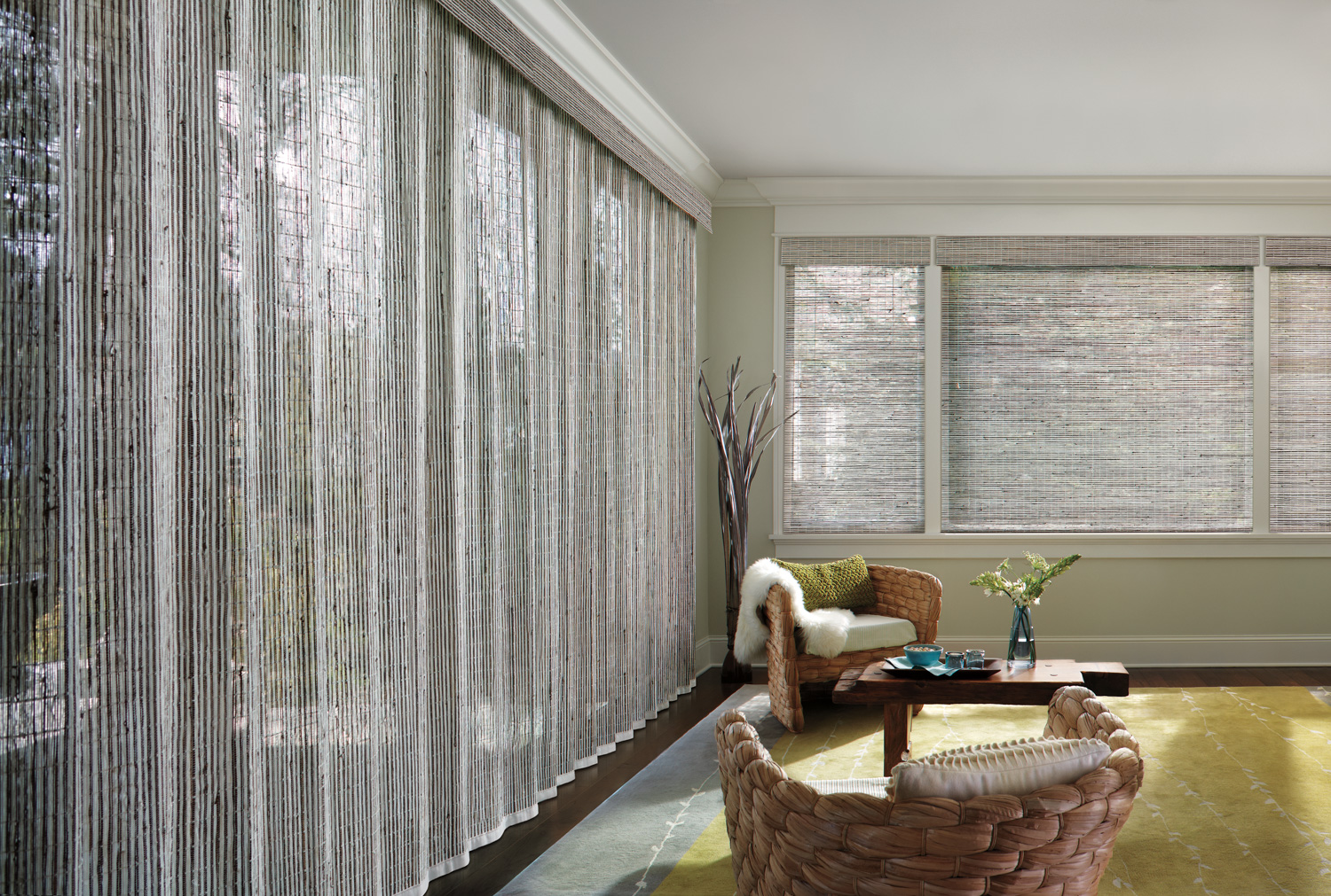 A cozy living room with a window covered in blinds made of vertical woven wood Roman shades.