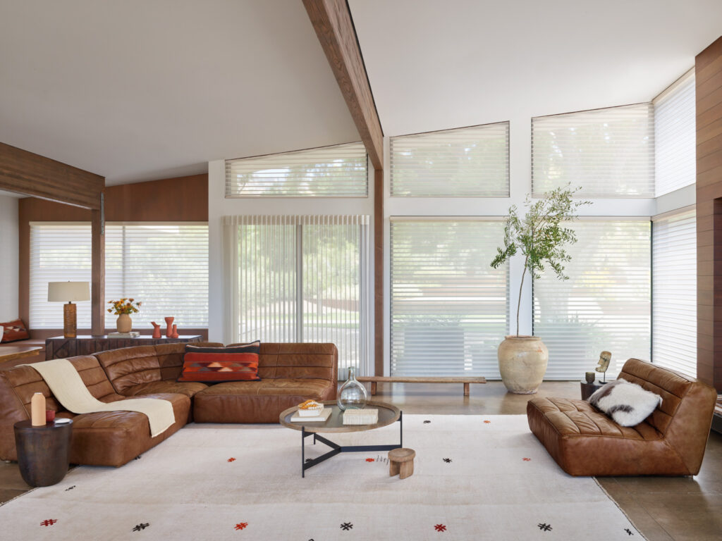 A modern living room with leather furniture and large windows, featuring Hunter Douglas Silhouette® Sheer Shades in specialty shaped windows.