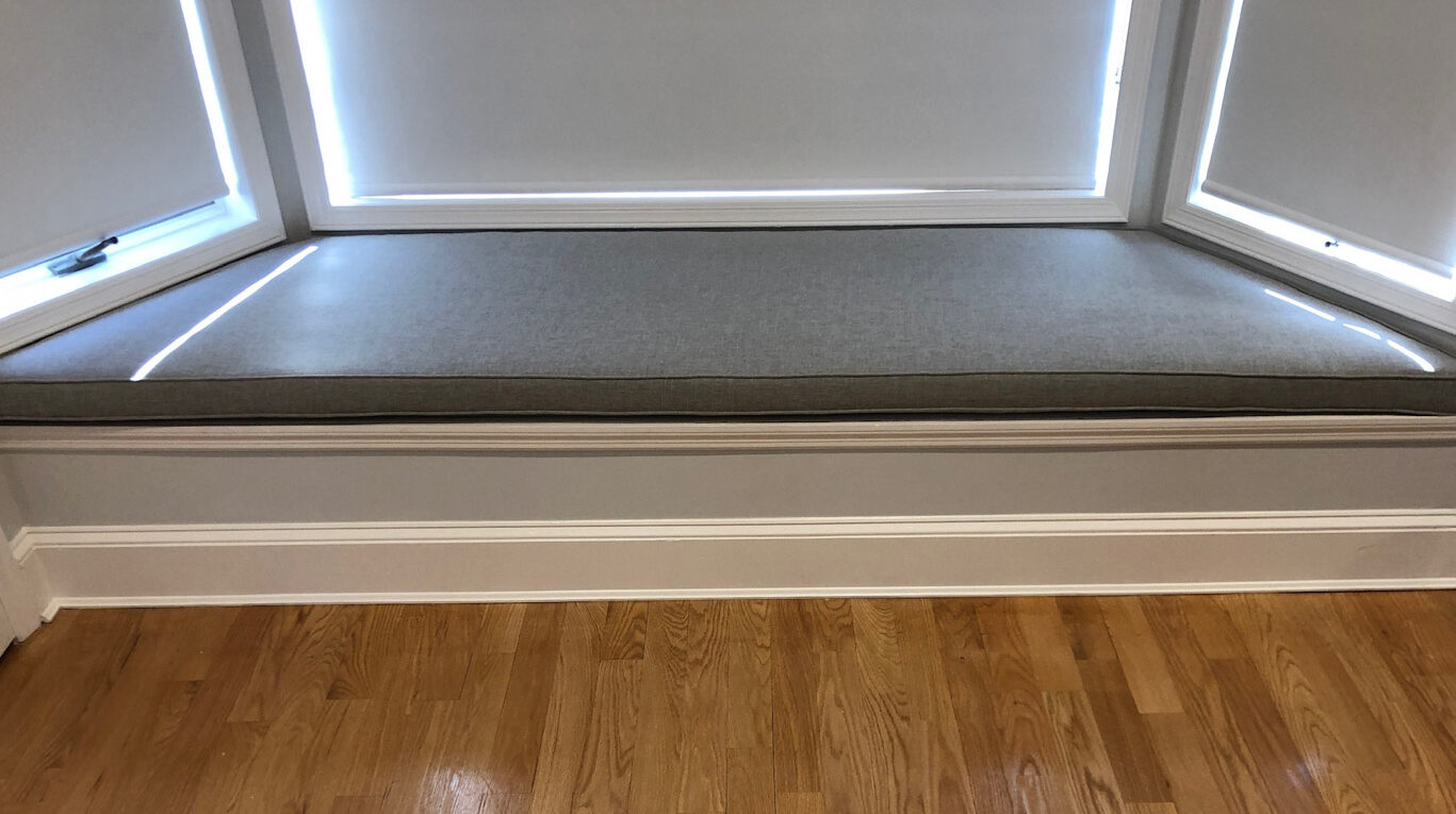 Custom upholstered bench cushion on a cozy window seat with a soft light illuminating the area.