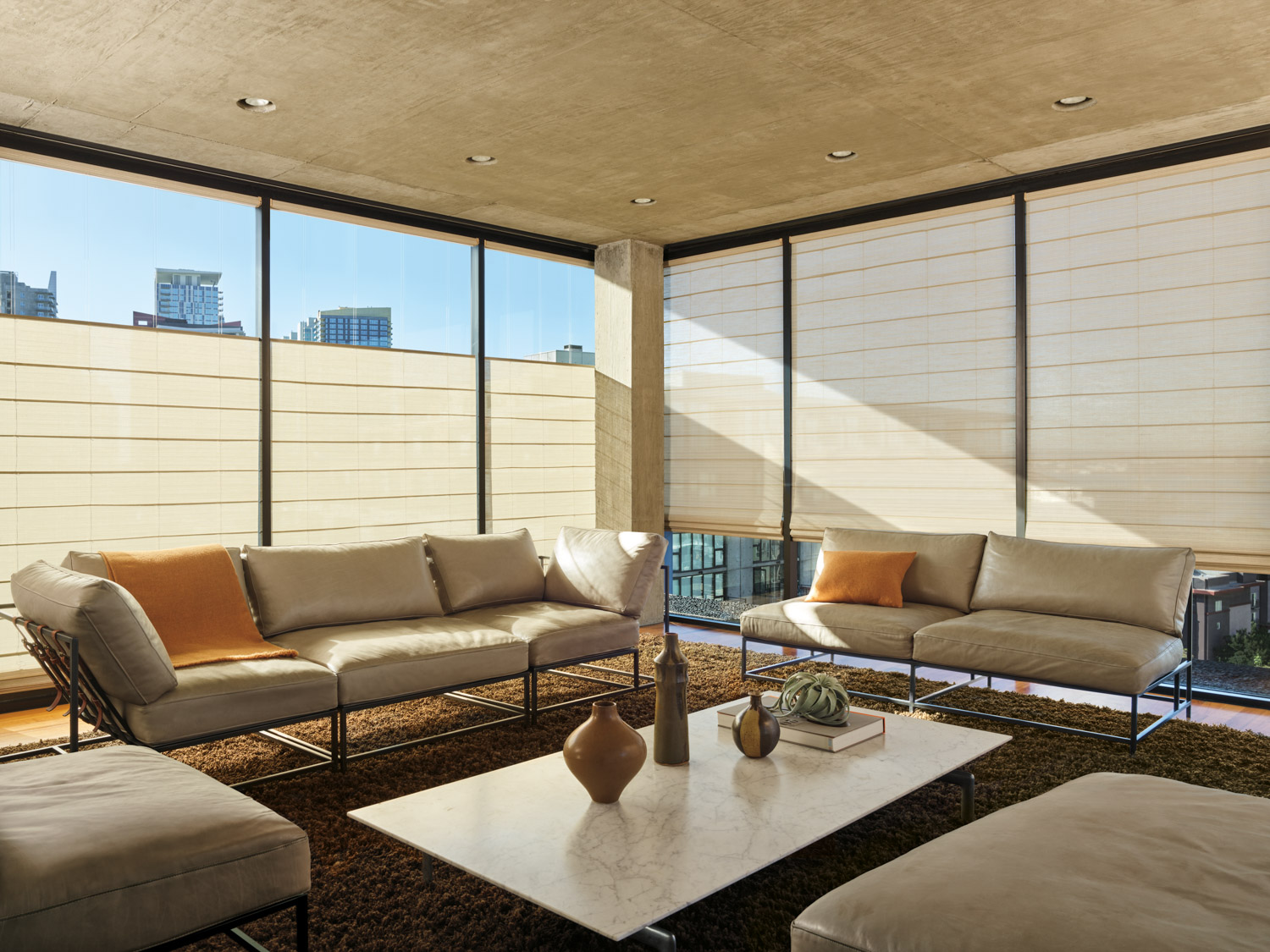 Hunter Douglas Alustra® Woven Textures® Roman Shades in a living room with large windows and furniture.