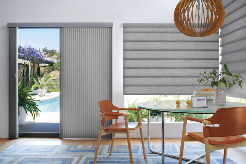 A dining room with a table and chairs in front of a sliding glass door, featuring Hunter Douglas Duette® Honeycomb Vertiglide Shades.