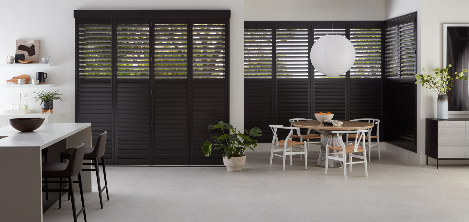 A kitchen with black shutters and white walls, featuring wood shutters on large windows.