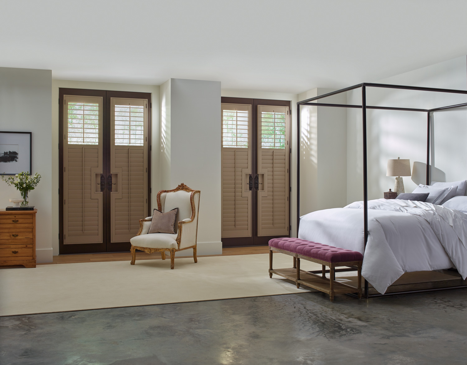 A cozy bedroom with a canopy bed and a chair. Wood shutters on doors with cut outs for handles.