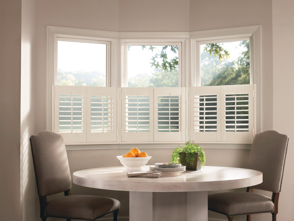 A bay window with Hunter Douglas NewStyle® Hybrid Shutters and a table.