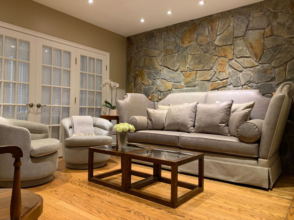 Stone wall living room featuring reupholstered sofa and swivel chairs.