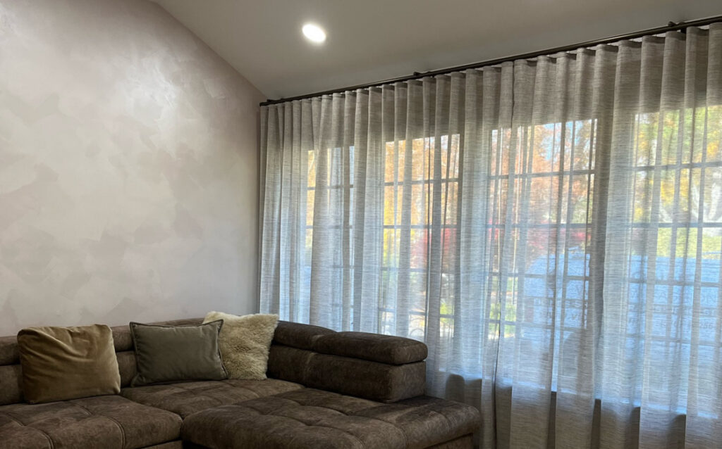 A stylish living room featuring a comfortable couch and beautiful ripple fold style sheer curtains.